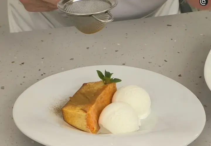 Un trozo de flan de calabaza Arguiñano, espolvoreado con canela, acompañado de dos bolas de helado de vainilla y una hoja de menta.