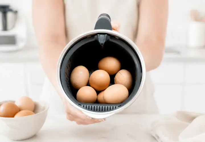 Manos sostienen el recipiente de la Thermomix lleno de huevos, listos para cocer huevos thermomix.