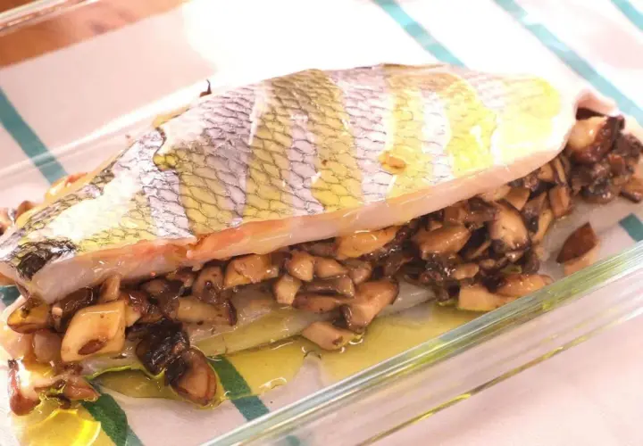 Pescado relleno de setas al horno, jugoso y dorado, listo para servir en una fuente de cristal.