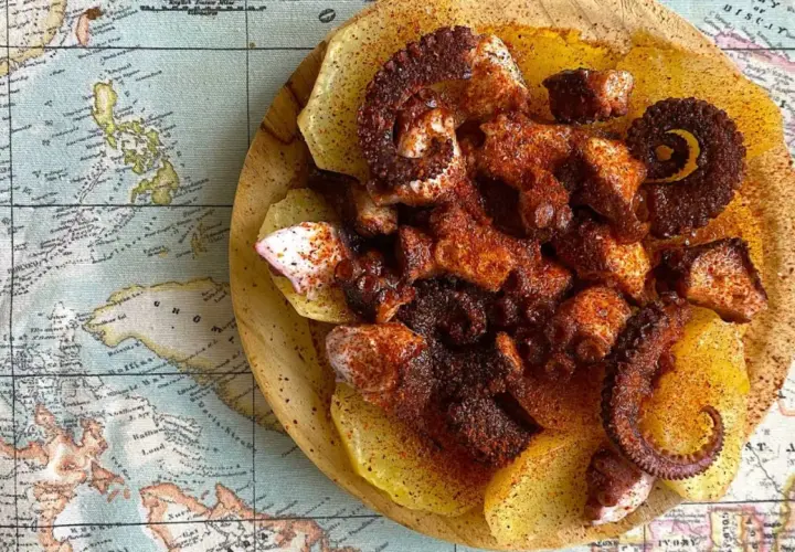 Pulpo con patatas, un plato gallego servido sobre un mapa antiguo. Tentáculos de pulpo especiados y tiernos sobre rodajas de patata.
