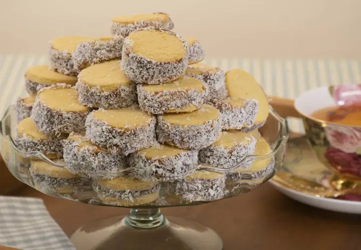 Montón de alfajores de maicena cubiertos de coco rallado, apilados en una fuente de vidrio.
