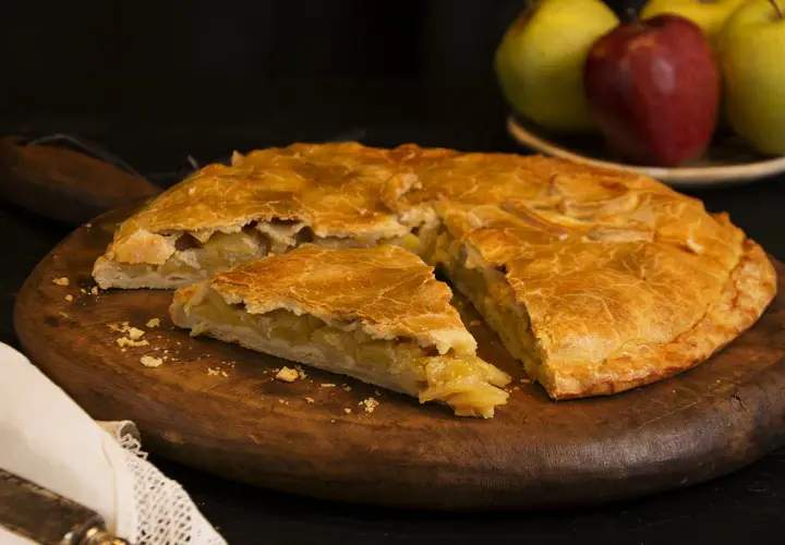 Empanada de manzana de la abuela, dorada y casera, servida en tabla de madera.