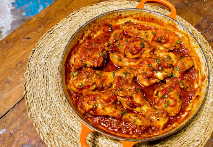 Pollo en salsa roja, como las recetas de pollo en salsa de la abuela, servido en cazuela naranja sobre esterilla de mimbre.