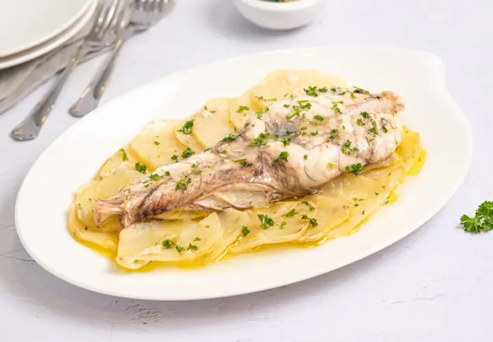 Rape al horno servido sobre patatas laminadas y espolvoreado con perejil fresco. Un plato sencillo y delicioso.