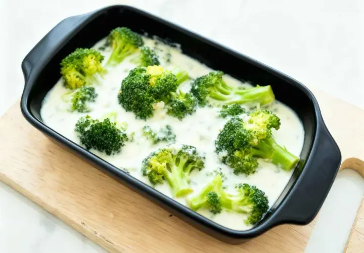 Brocoli con bechamel cremoso en una bandeja negra, listo para hornear. Un plato reconfortante y delicioso.