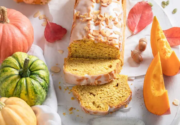 Bizcocho de calabaza Thermomix cubierto de glaseado y almendras. Rodeado de calabazas, hojas de otoño y bellotas.
