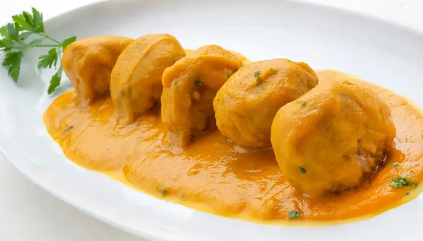 Cinco albóndigas en salsa arguiñano, servidas en un plato blanco con perejil fresco.