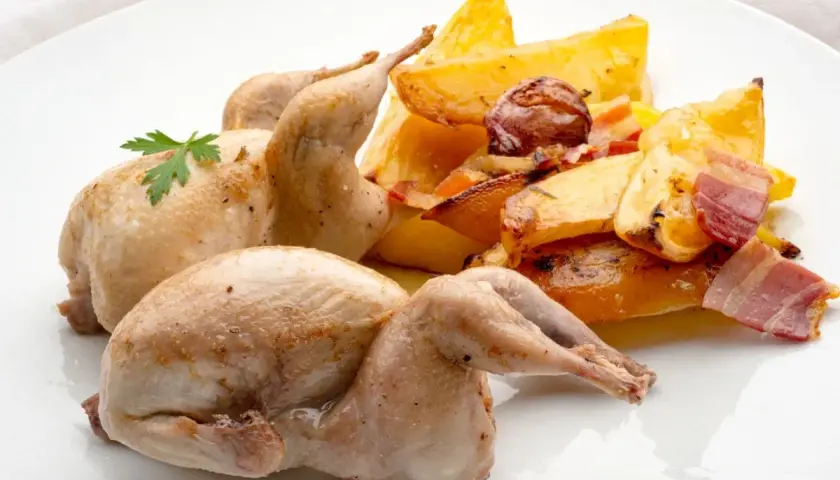 Dos codornices al horno, doradas y jugosas, acompañadas de patatas rústicas asadas con tocino y hierbas.