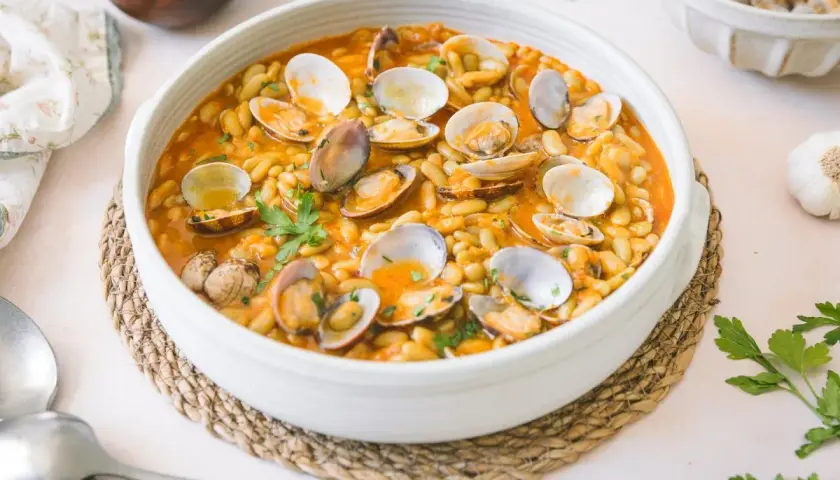 Plato de verdinas con almejas en salsa, decorado con perejil fresco. Un festín marinero y vegetal.