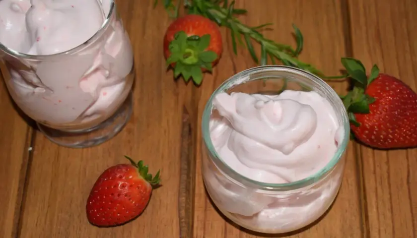 Delicioso postre con fresas, cremoso y ligero, servido en copas. Fresas frescas y romero decoran la mesa de madera.