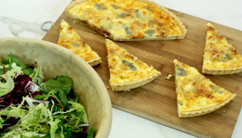 Un delicioso pastel de puerros recién horneado, cortado en porciones, junto a una ensalada fresca en un cuenco de madera.