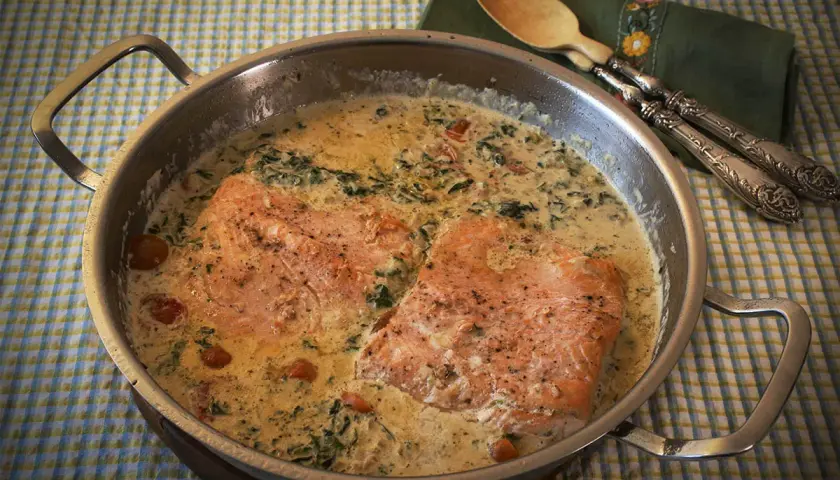 Dos filetes de salmón a la toscana en una sartén con salsa cremosa, espinacas y tomates cherry.