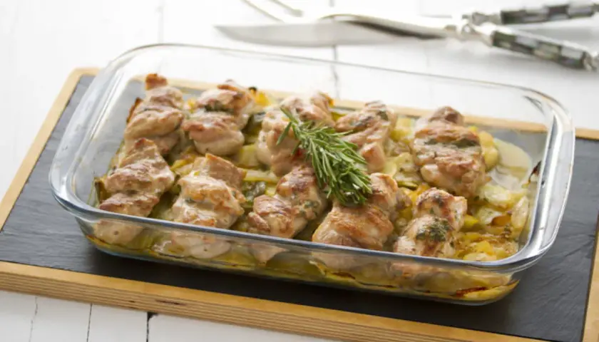 Contramuslos de pollo al horno crujientes, dorados y jugosos, servidos en una fuente de cristal con patatas y romero.