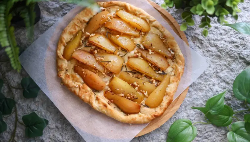 Deliciosa tarta de pera rústica, con trozos de pera caramelizada, nueces y romero, sobre una base dorada y crujiente.