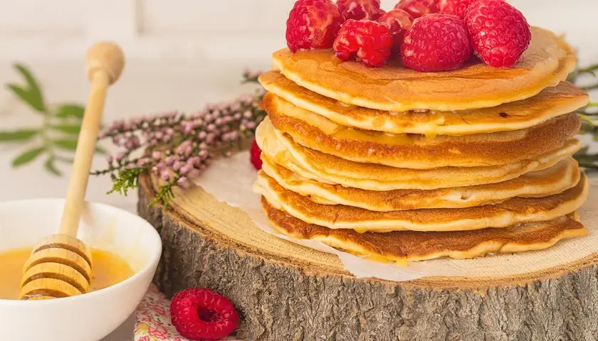 Una pila de tortitas de avena doradas, cubiertas con frambuesas frescas y miel, listas para disfrutar.