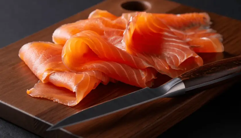 Finas lonchas de salmón ahumado sobre tabla de madera. Se puede congelar el salmón ahumado para conservarlo fresco.