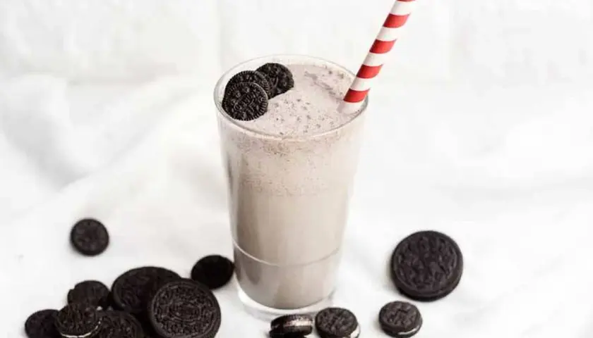 Delicioso batido de oreo cremoso, adornado con galletas enteras y trozos, listo para disfrutar con su pajita a rayas.