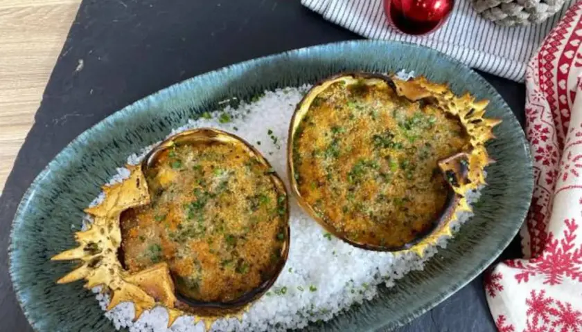 Dos deliciosos txangurros a la donostiarra, gratinados y espolvoreados con perejil, reposan sobre sal gruesa en un plato festivo.