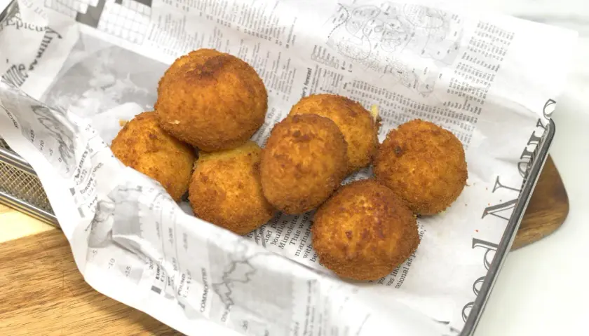 Croquetas de gambas doradas y crujientes, servidas sobre papel de periódico en una cesta metálica.