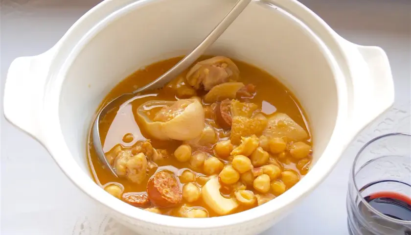 Un plato humeante de callos a la gallega, con garbanzos, chorizo y trozos de carne en una cazuela blanca.