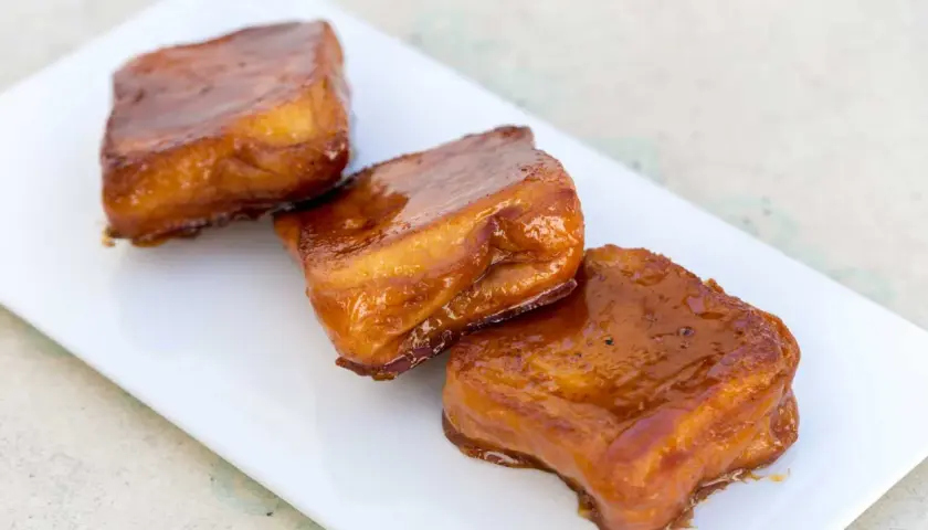 Tres torrijas de miel, doradas y brillantes, servidas en un plato blanco.