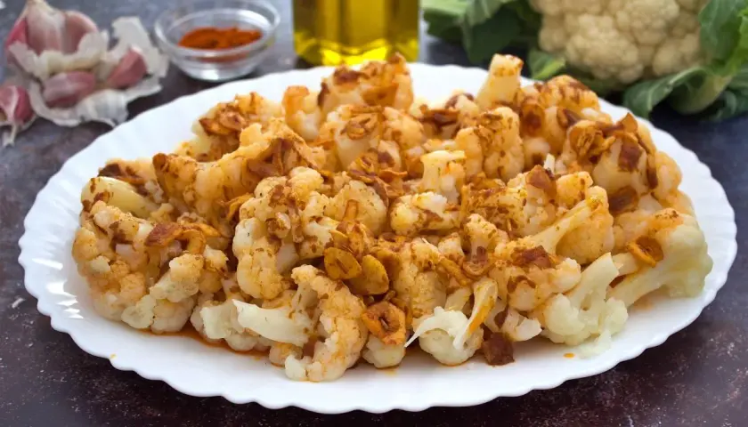 Coliflor al ajoarriero, con trozos dorados de ajo y pimentón, servida en un plato blanco.