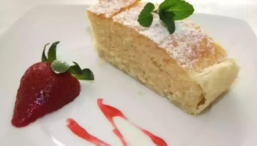Un delicioso bizcocho de almendras espolvoreado con azúcar glas, decorado con una fresa y menta.