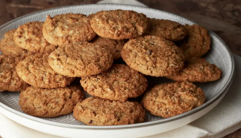 Montón de carajitos del profesor, galletas doradas y crujientes con avena y coco, apiladas en un plato gris.