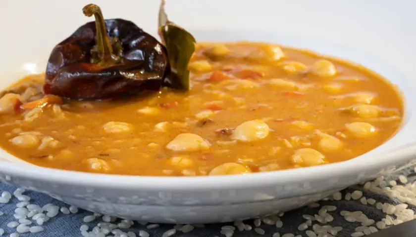 Un plato de garbanzos con arroz, reconfortante y sabroso, coronado con un pimiento seco y una hoja de laurel.