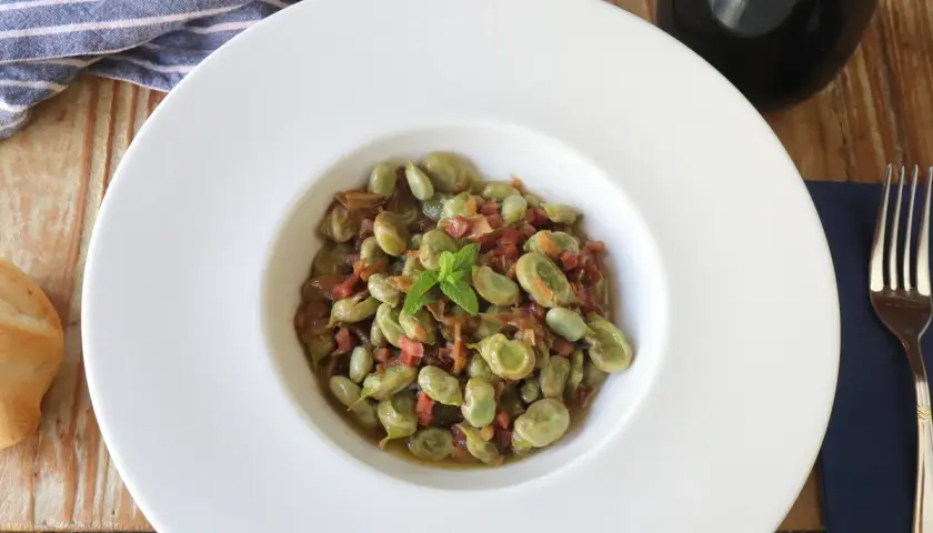 Plato de habas tiernas con jamón, ideal para tus recetas de habas. Servido en un cuenco blanco con menta fresca.