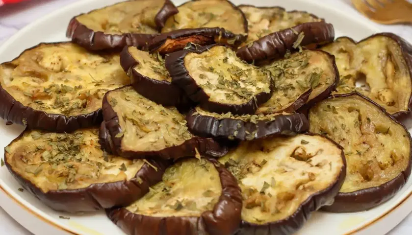 Rodajas de berenjenas al horno, doradas y espolvoreadas con hierbas aromáticas, listas para disfrutar.
