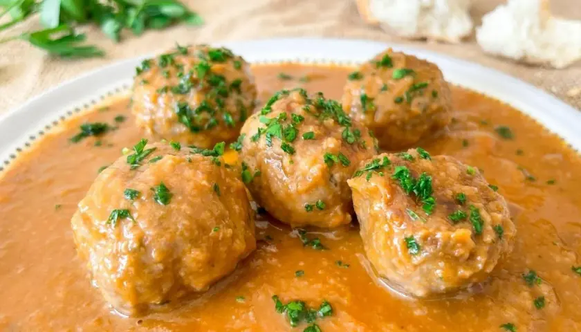 Cinco deliciosas albóndigas al horno en una rica salsa, espolvoreadas con perejil fresco. ¡Perfectas para mojar pan!