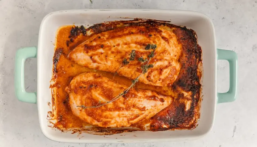 Dos jugosos solomillos de pavo al horno, dorados y con hierbas, reposan en una fuente blanca con asas turquesa.