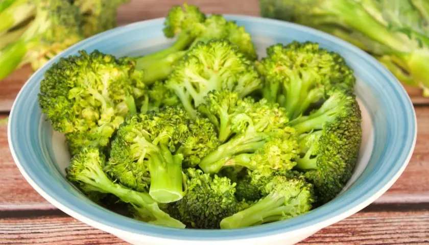 Brocoli al microondas en un cuenco azul sobre madera.