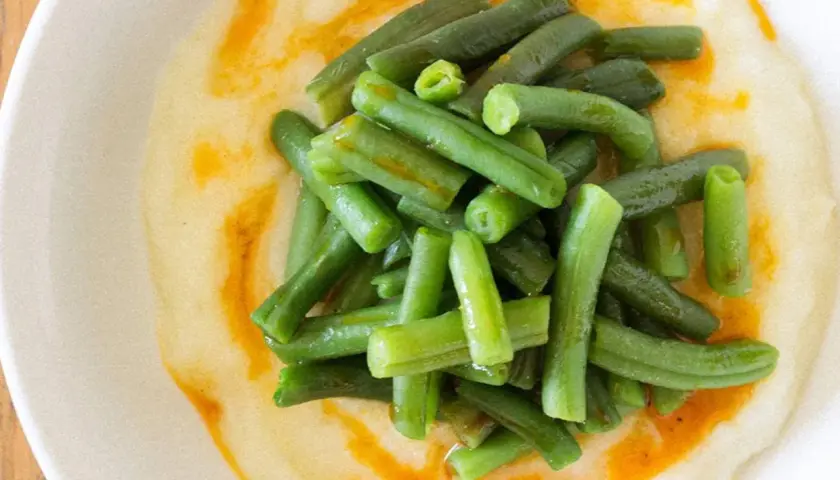 Judías verdes frescas y tiernas sobre una cremosa base de puré de patatas, con un toque de aceite de pimentón.