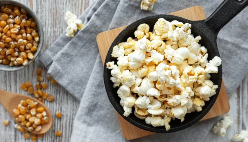 Palomitas recién hechas en sartén, listas para disfrutar. Maíz de palomitas en un cuenco y cuchara de madera.