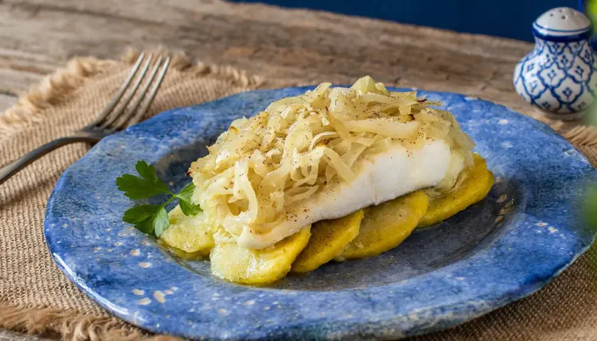 Delicioso bacalao a la portuguesa, servido sobre patatas y cubierto con cebolla caramelizada.