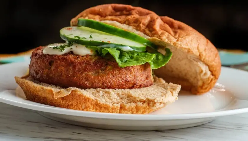 Deliciosa hamburguesa de salmón con lechuga, pepino y salsa cremosa en un pan tostado.