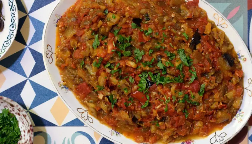 Un plato de pisto con berenjena, lleno de verduras cocidas y espolvoreado con perejil fresco.