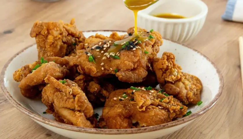 Crujiente pollo frito coreano bañado en salsa dorada, espolvoreado con semillas de sésamo y cebollín. ¡Un bocado irresistible!