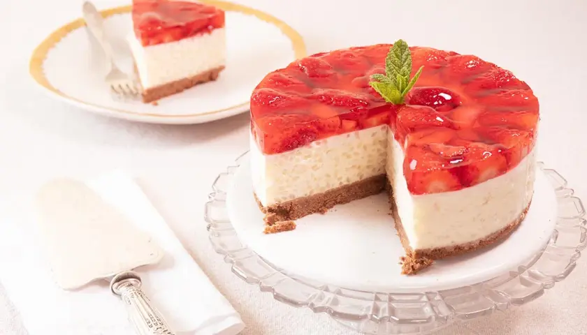 Deliciosa tarta de fresa con una capa cremosa y cobertura de gelatina de fresa, decorada con menta. Una porción ya servida en un plato.