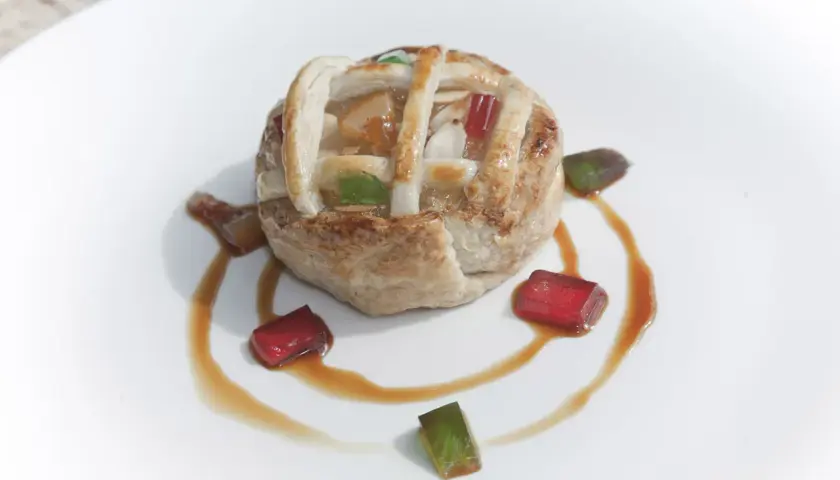 Deliciosa tarta de Mondoñedo, con su masa dorada y relleno de frutas, decorada con gominolas de colores y un sirope dulce.