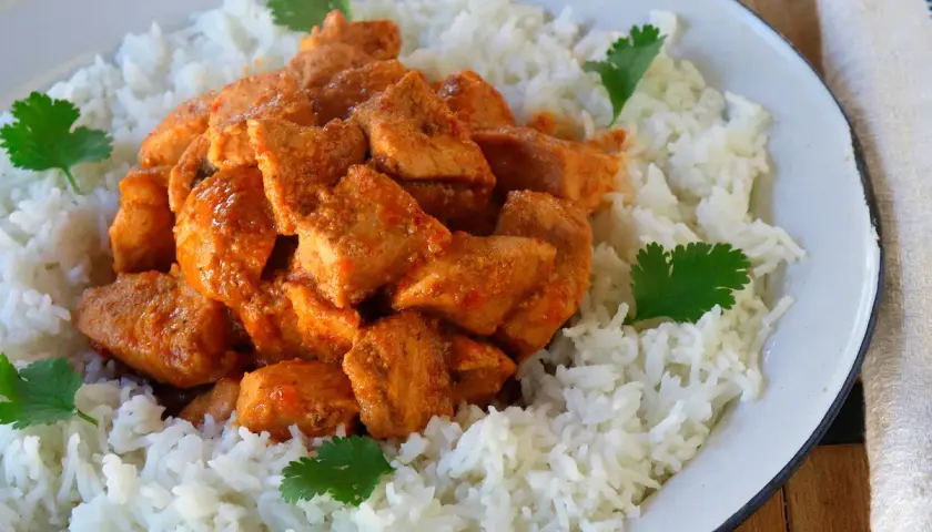 Sabroso pollo tikka masala servido sobre una cama de arroz blanco, decorado con hojas de cilantro fresco.
