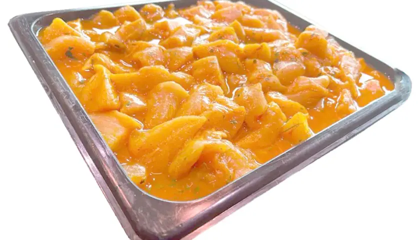 Bandeja metálica llena de trozos de pollo marinados en una salsa anaranjada, listos para convertirse en deliciosos pinchitos.