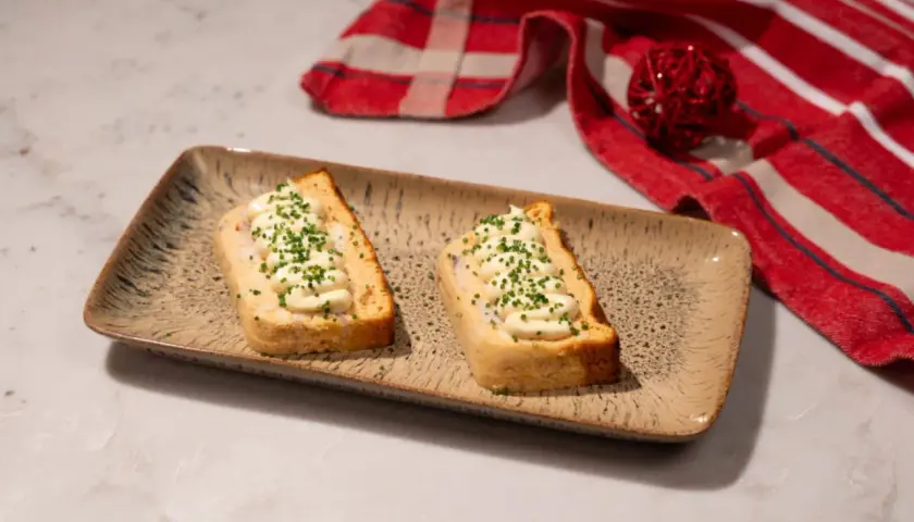 Dos porciones de pastel de cabracho, cubiertas con mayonesa y cebollino, servidas en una bandeja rústica.