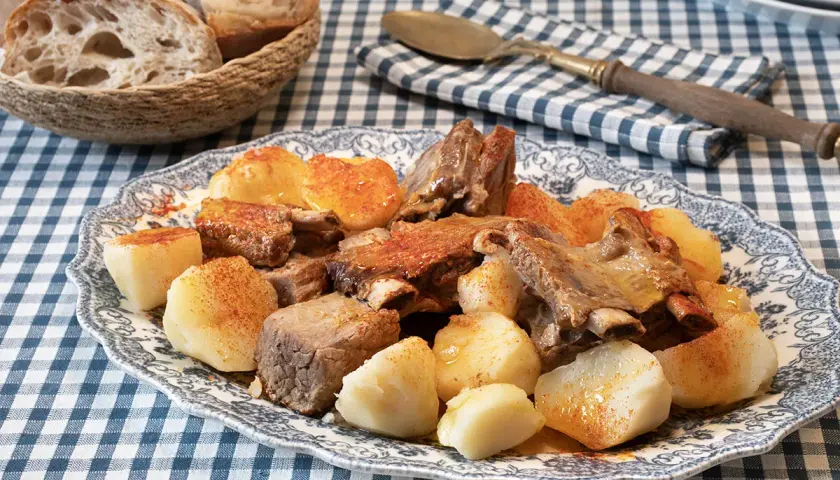 Un plato de carne o caldeiro con patatas cocidas y pan rústico en una cesta.