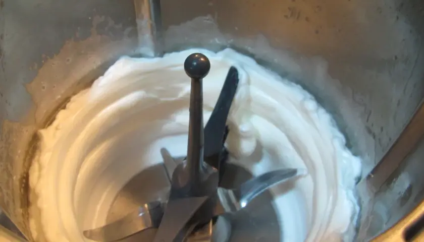 Montar claras a punto de nieve en Thermomix. La mezcla cremosa y blanca rodea las cuchillas.