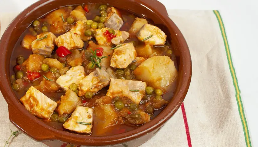 Un apetitoso marmitako de salmón, con trozos de pescado, patatas, guisantes y pimientos rojos, servido en cazuela de barro.