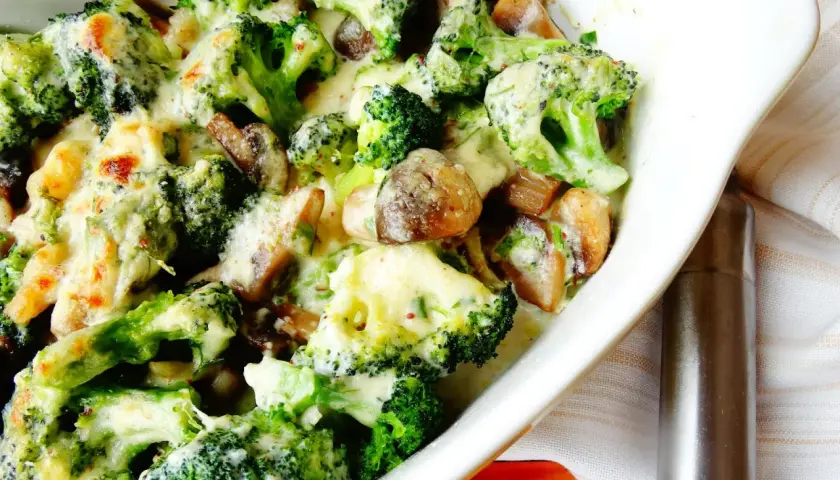 Brocoli con champiñones gratinados en una cazuela blanca, cubiertos de una cremosa salsa de queso.