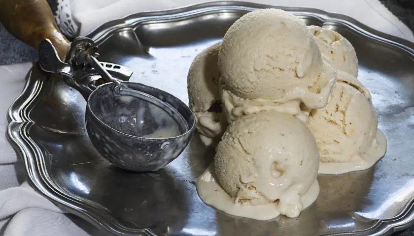 Cremoso helado de plátano derritiéndose en una bandeja de plata, junto a un cucharón.
